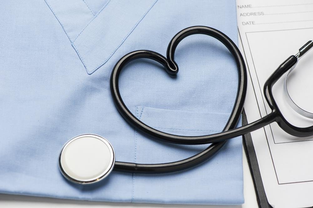 Fonendoscopio nero col tubo piegato a cuore su una casacca sanitaria azzurra, accanto a un modulo bianco